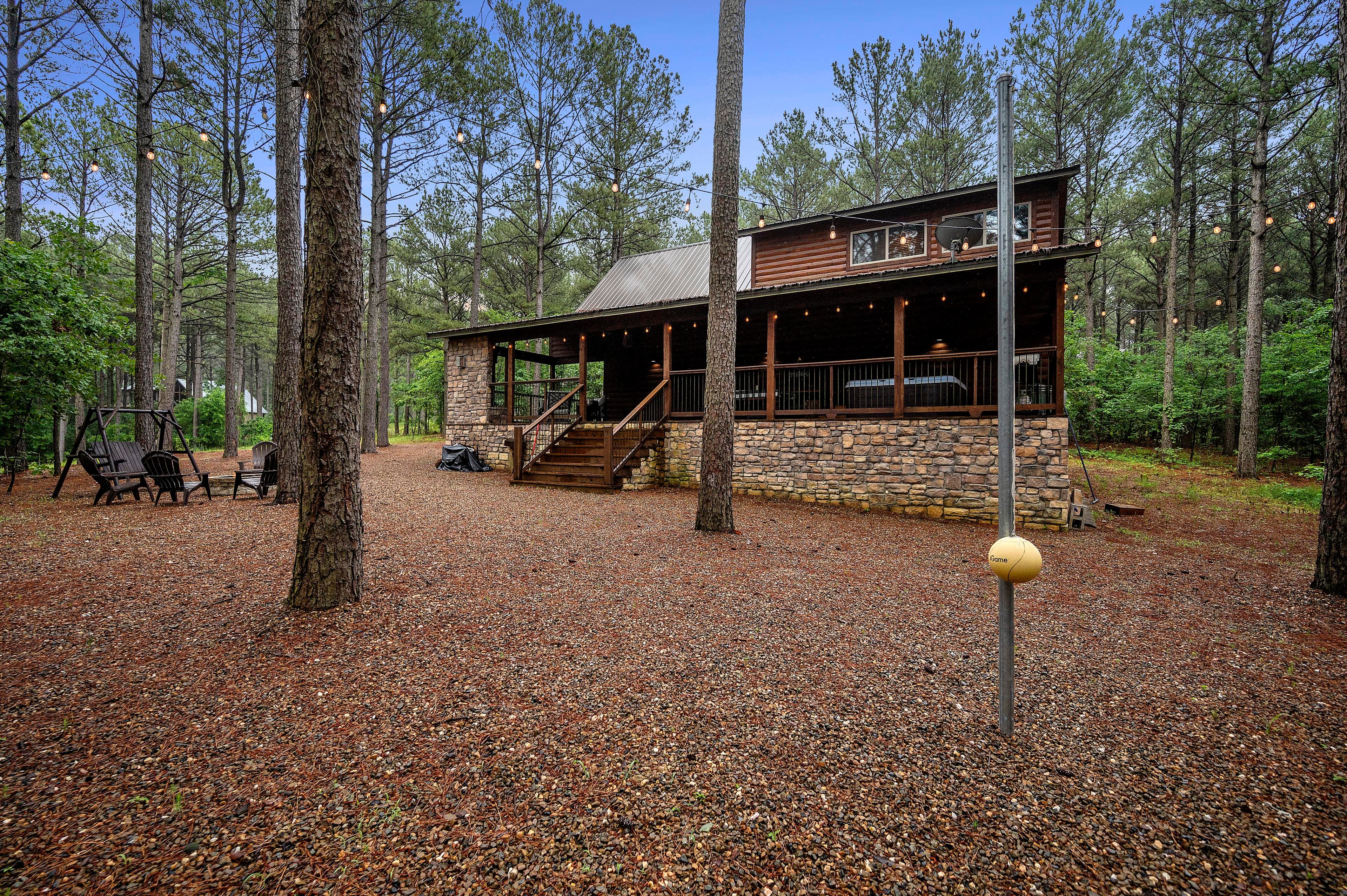 A rustic cabin surrounded by tall pine trees and a gravel pathway.