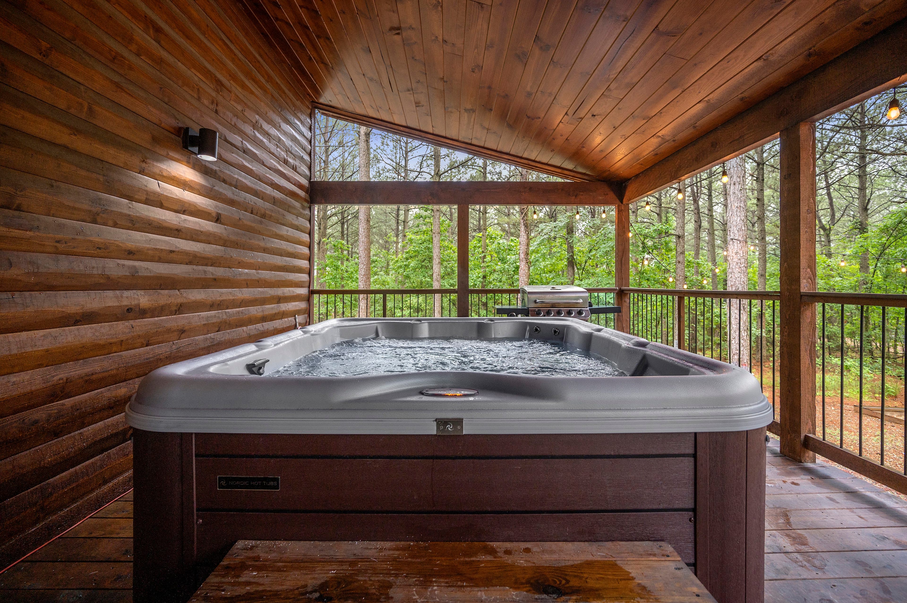 A hot tub with bubbling water is situated on a wooden deck surrounded by trees.