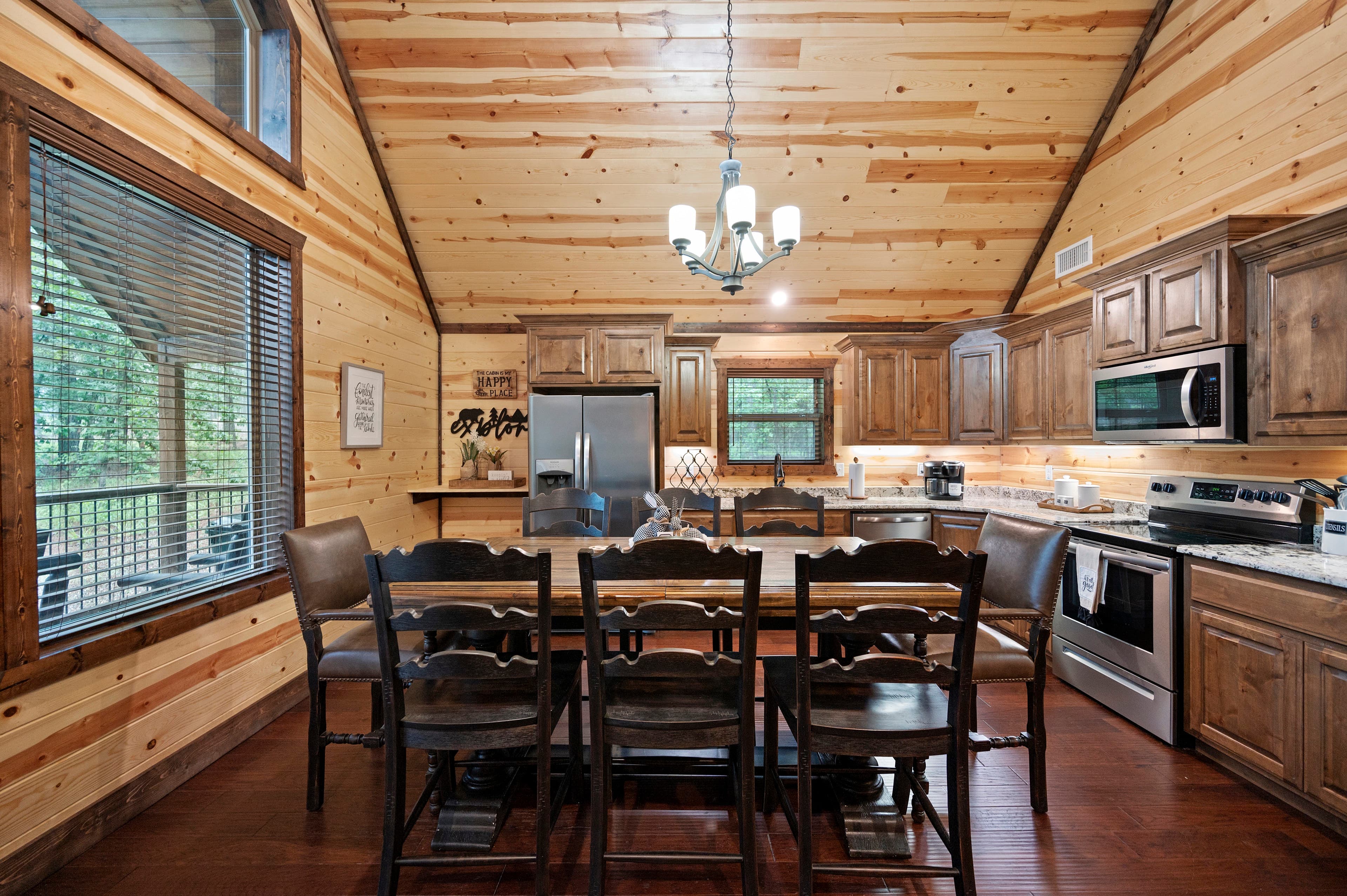 A wooden kitchen and dining area with a large table, stainless steel appliances, and natural light coming through the windows.