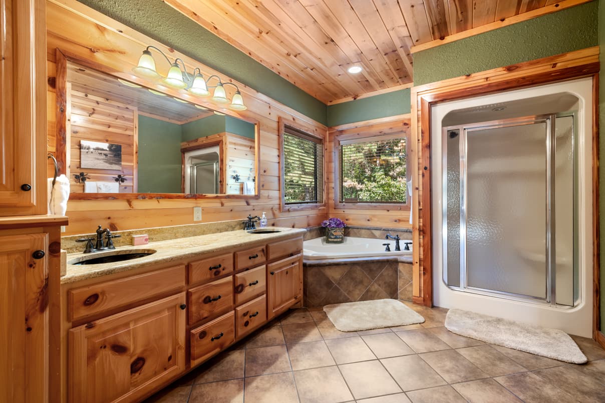 A spacious bathroom with wooden accents, a large mirror, a shower, and a soaking tub beside window views.