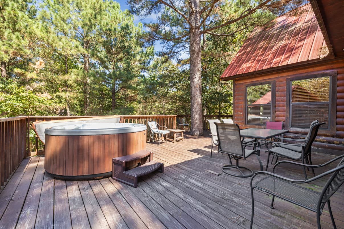A wooden deck featuring a hot tub, dining table, and chairs, surrounded by tall trees.
