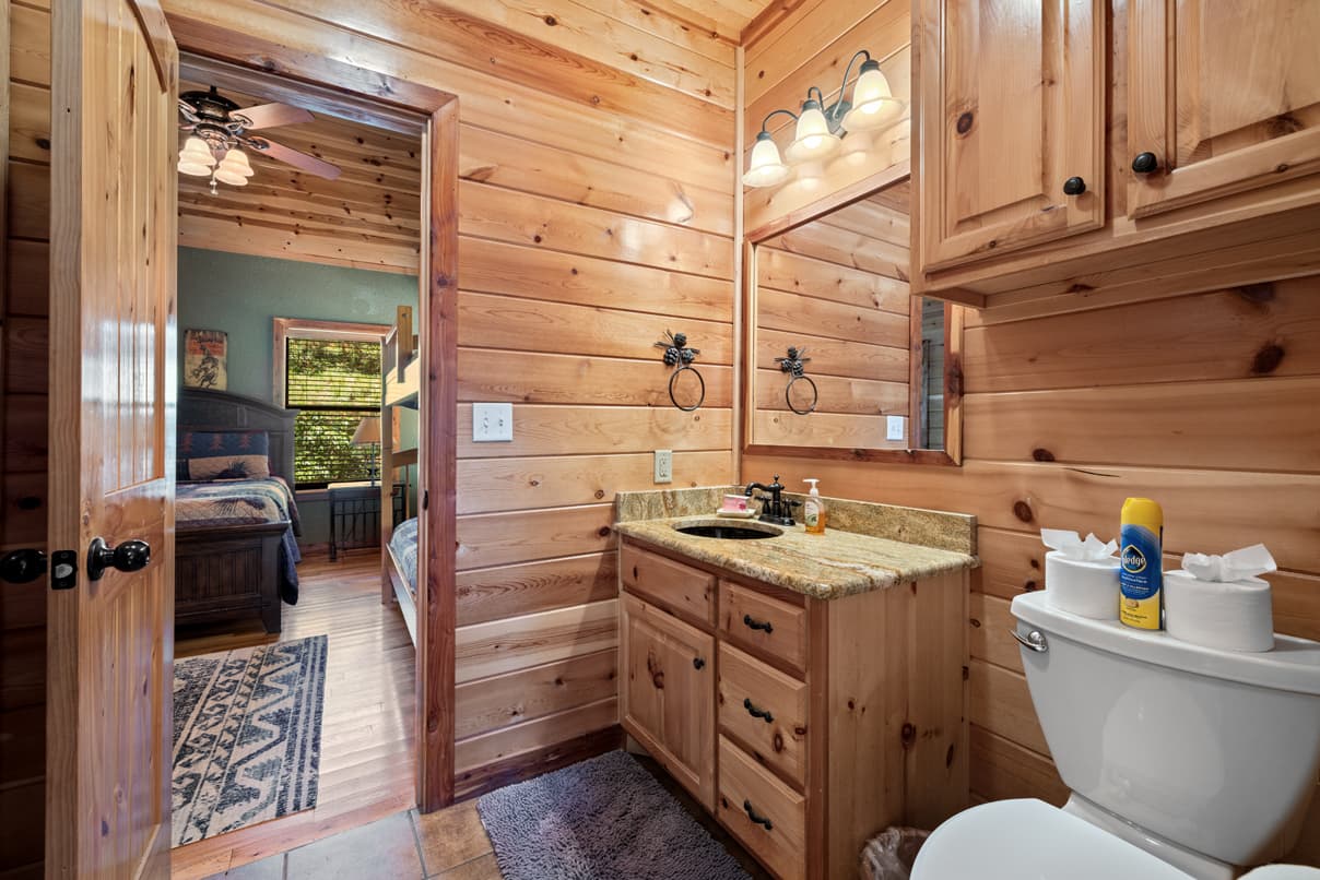 A rustic bathroom with wooden walls, a granite countertop, and a view of a bedroom beyond.