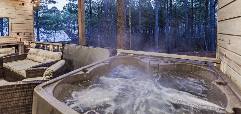 A hot tub with bubbling water on a deck surrounded by trees and a cozy seating area.