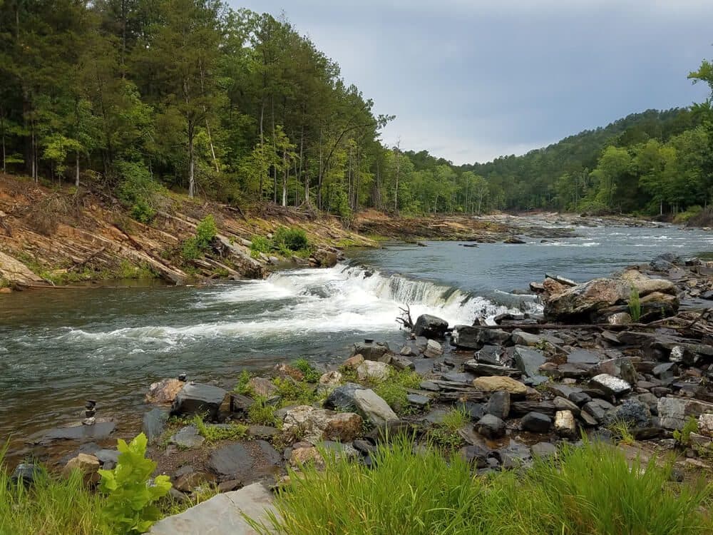 A serene river flows through a rocky landscape surrounded by lush green trees. A serene river flows through a rocky landscape surrounded by lush green trees.