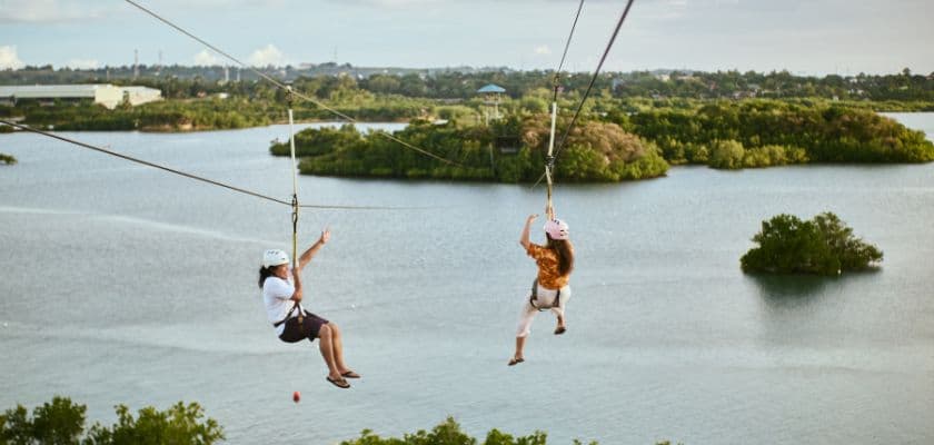 Two children ziplining over a scenic landscape with water and greenery.