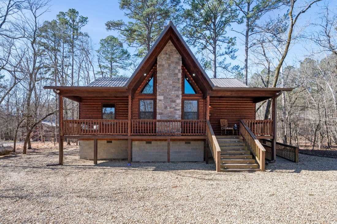 Front of log cabin with rock fireplace and large gravel driveway