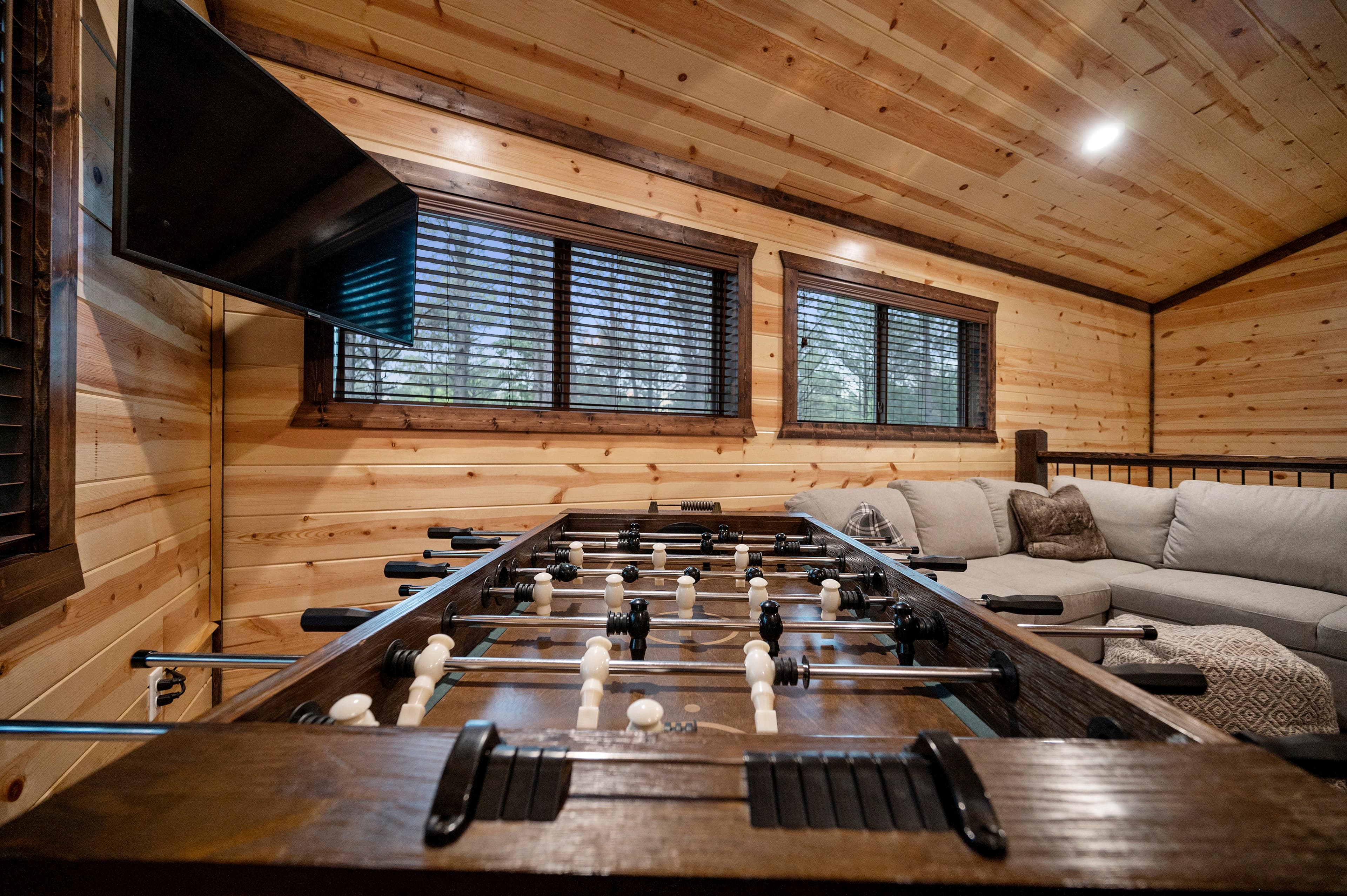 A cozy game room featuring a foosball table, large windows, and a comfortable seating area.