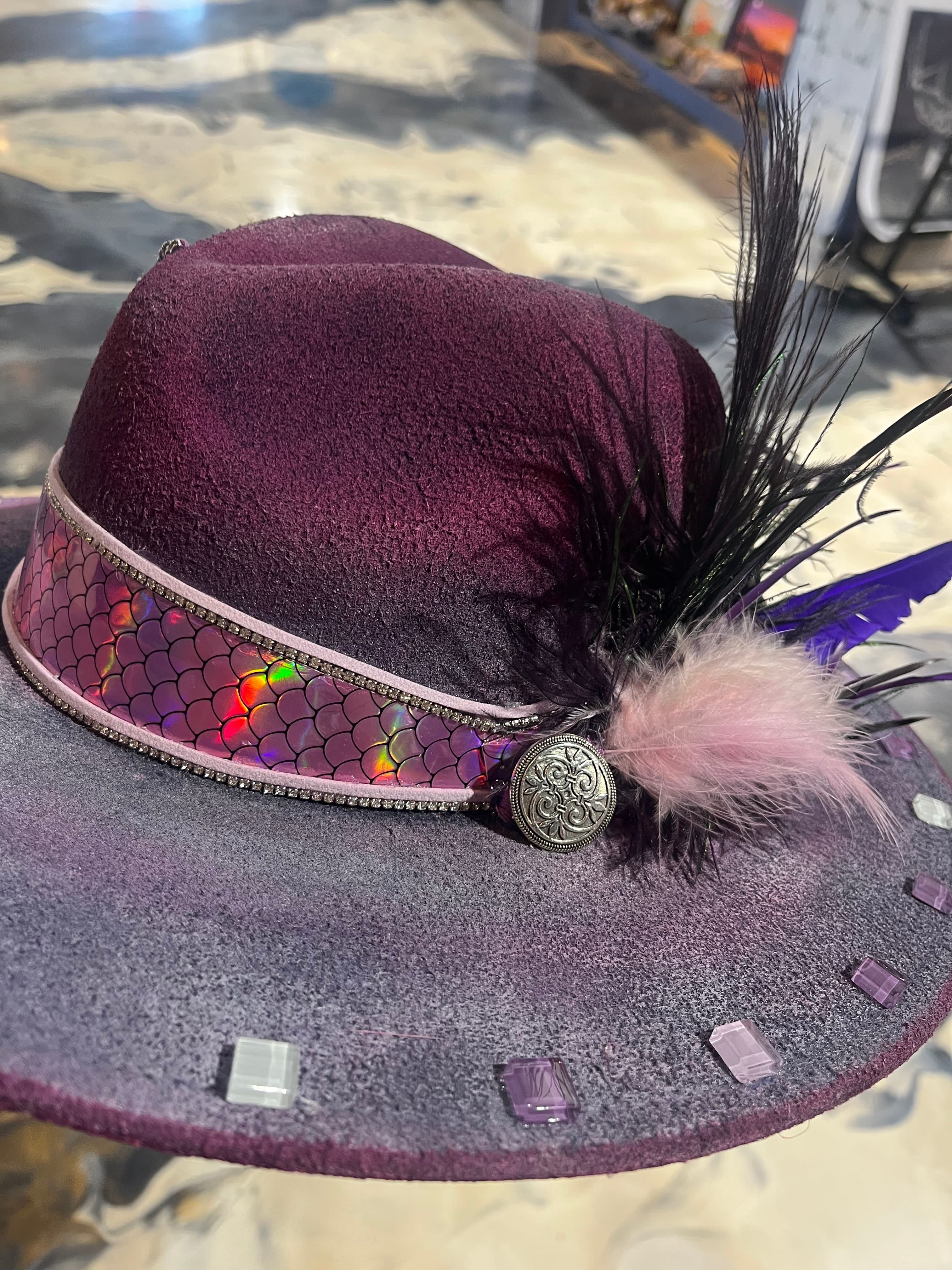 A stylish purple hat featuring a shimmering band, a feather, and decorative embellishments.
