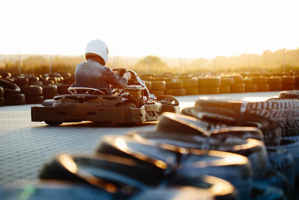 A go-kart racer speeds around the track at sunset, surrounded by tires.