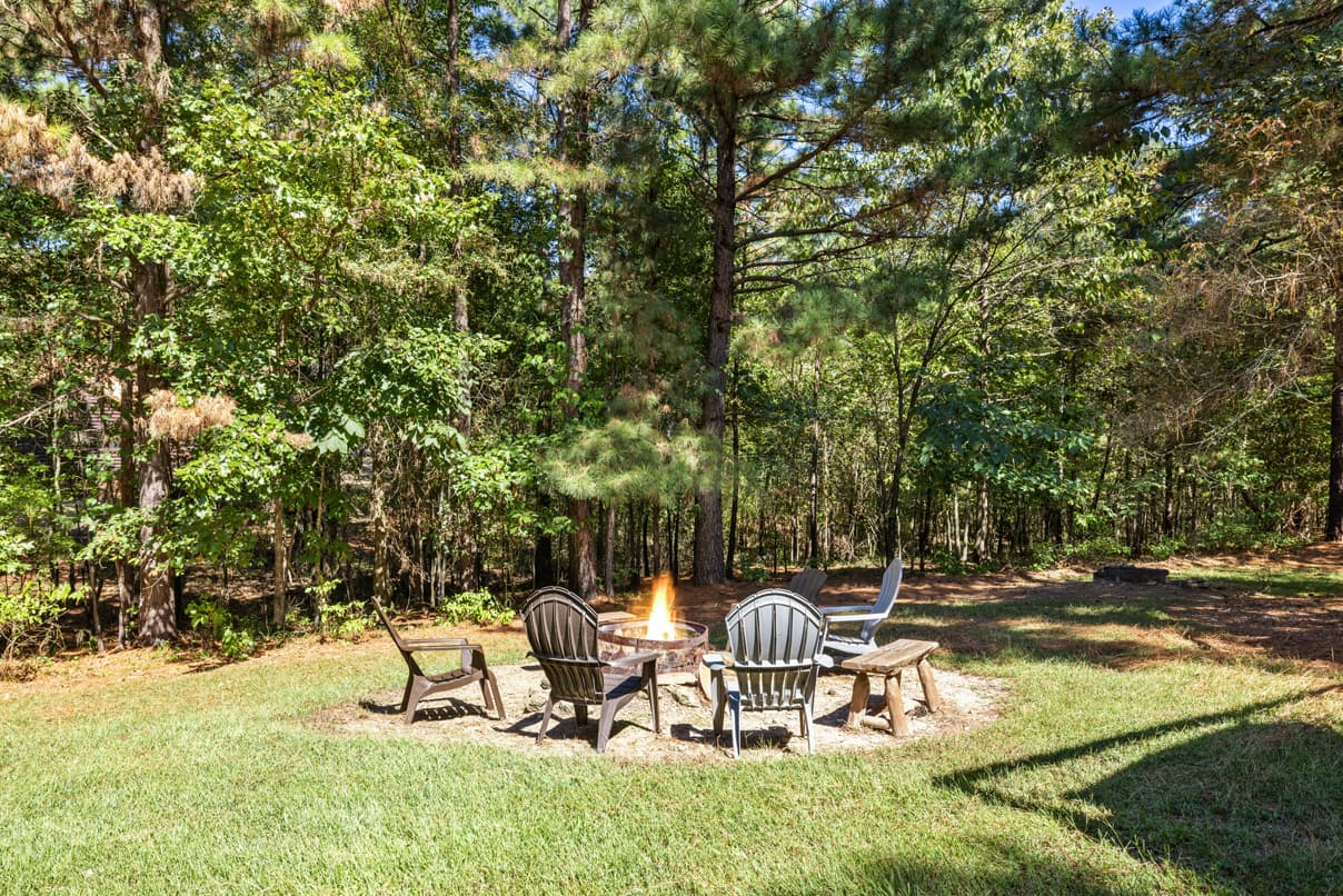 A fire pit surrounded by chairs in a wooded clearing.