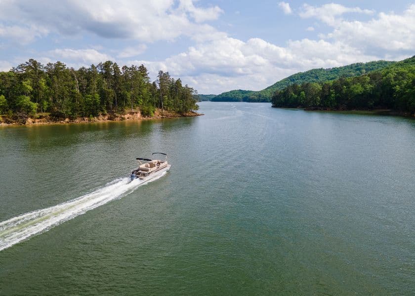 A boat glides along a calm lake surrounded by lush greenery and rolling hills under a partly cloudy sky. A boat glides along a calm lake surrounded by lush greenery and rolling hills under a partly cloudy sky.