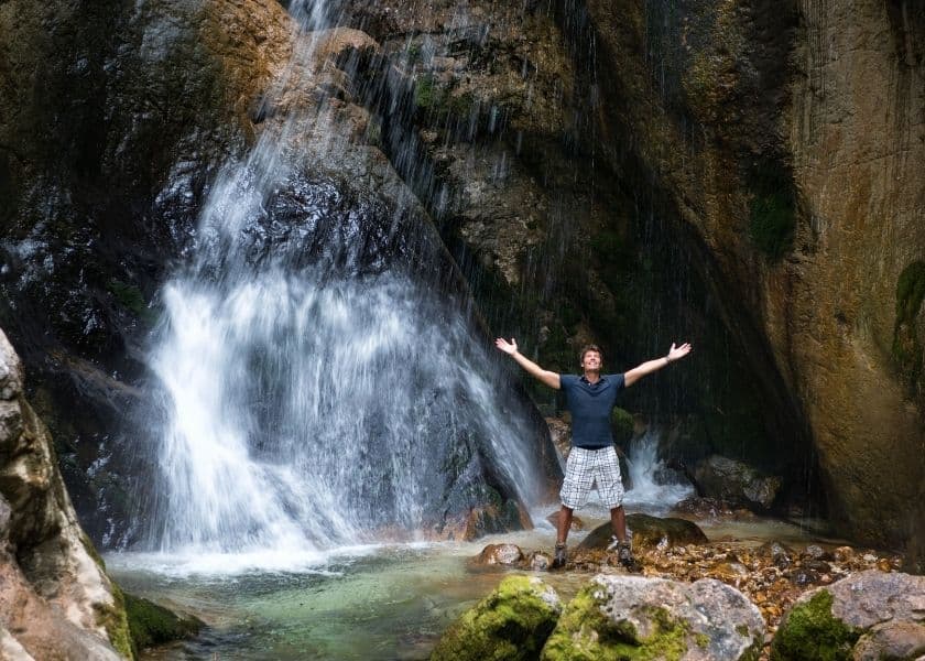 A person with outstretched arms stands joyfully in front of a waterfall. A person with outstretched arms stands joyfully in front of a waterfall.
