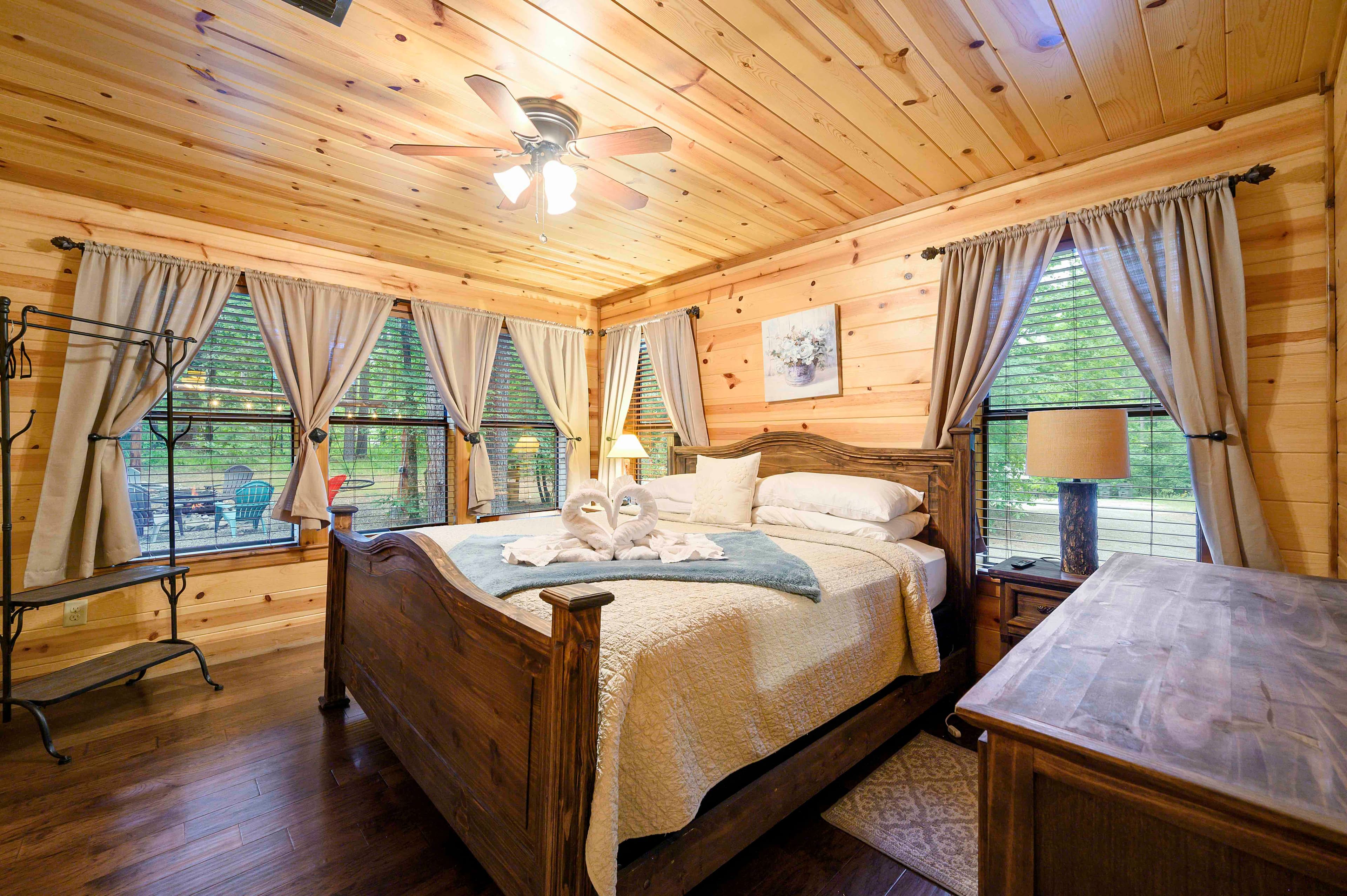 A cozy wooden bedroom with a queen-sized bed, large windows, and warm decor.