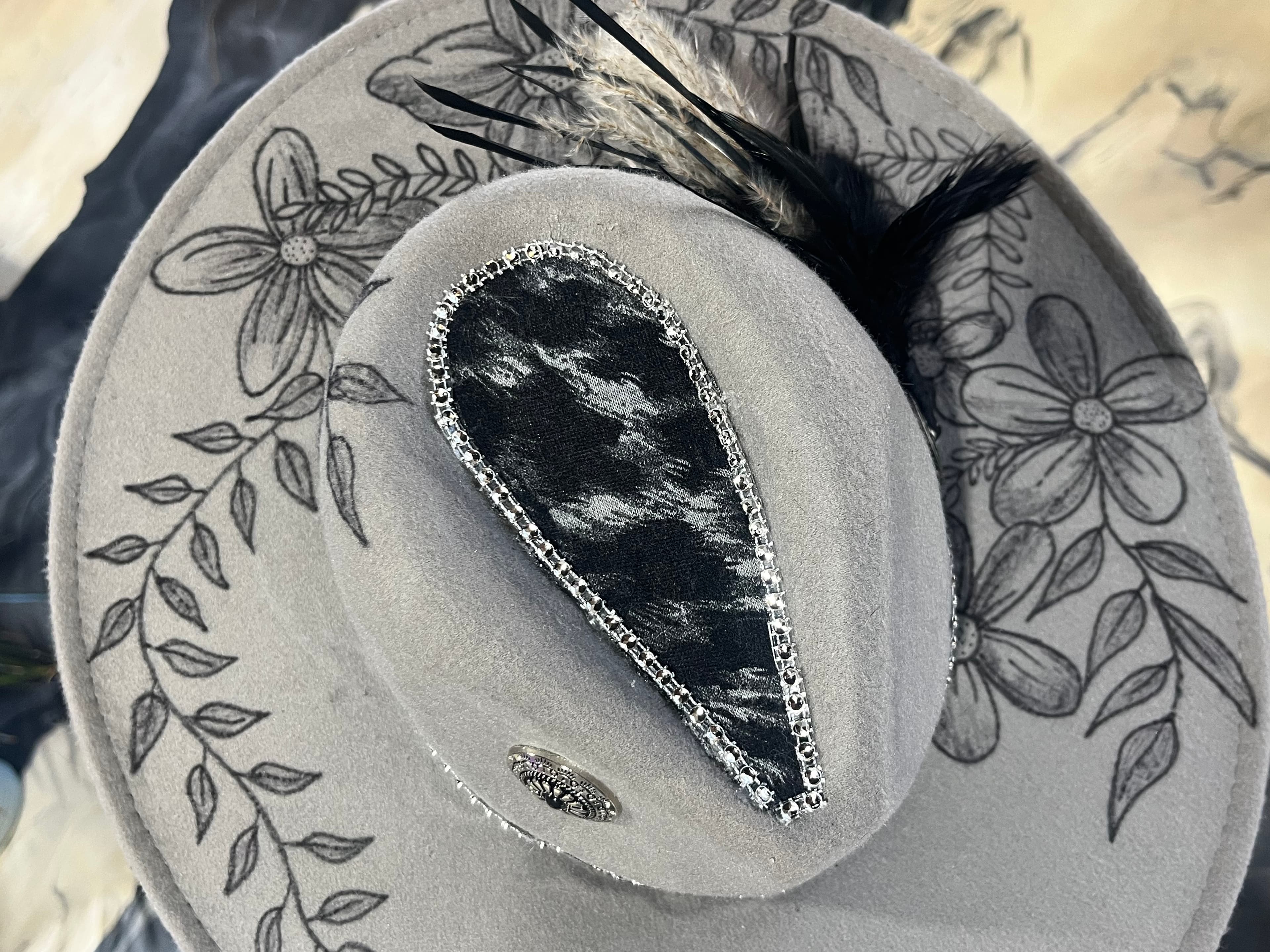 A gray hat adorned with floral designs and a decorative feather.