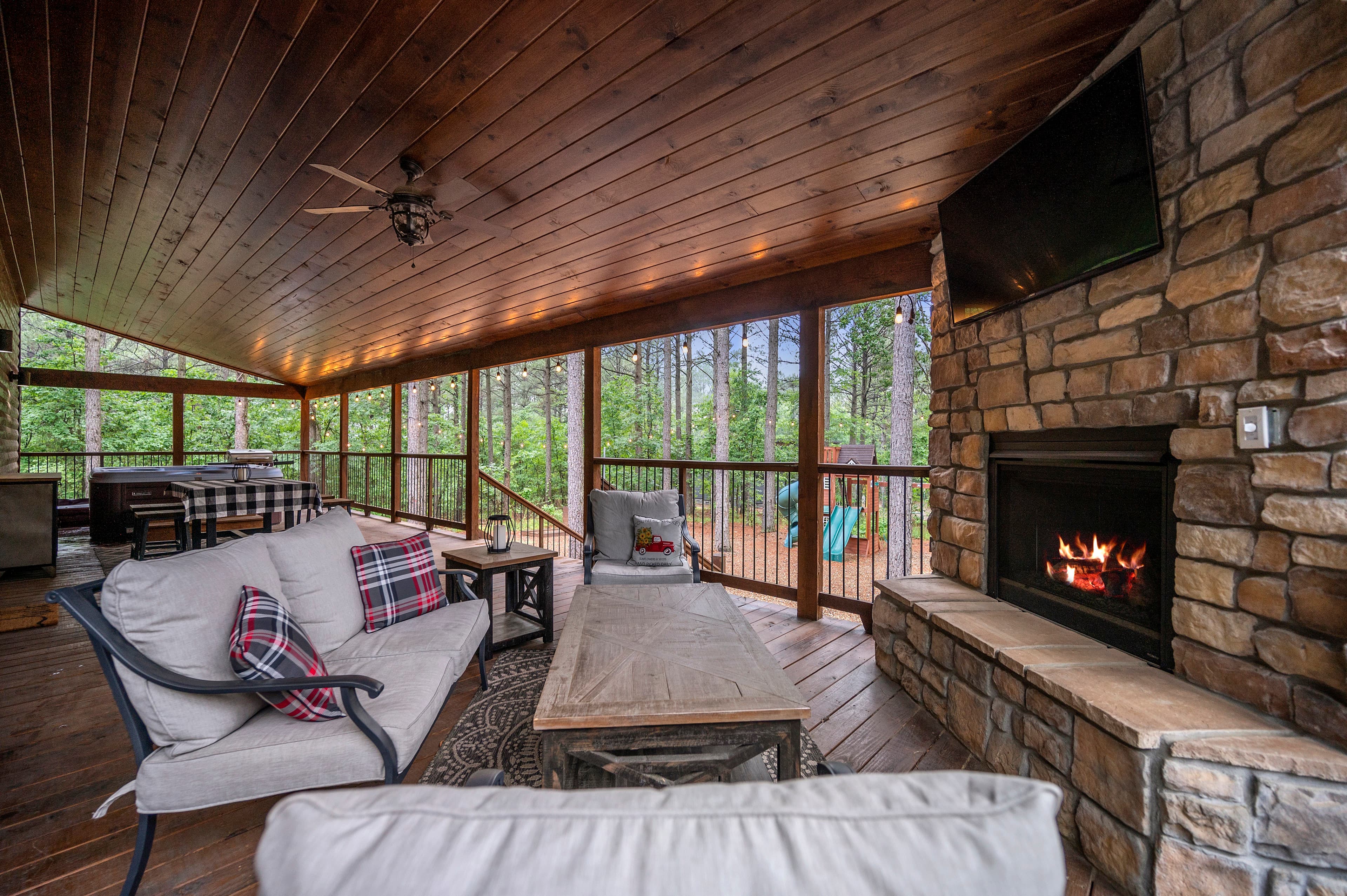 Cozy screened-in porch with stone fireplace, comfortable seating, and views of a forested area.