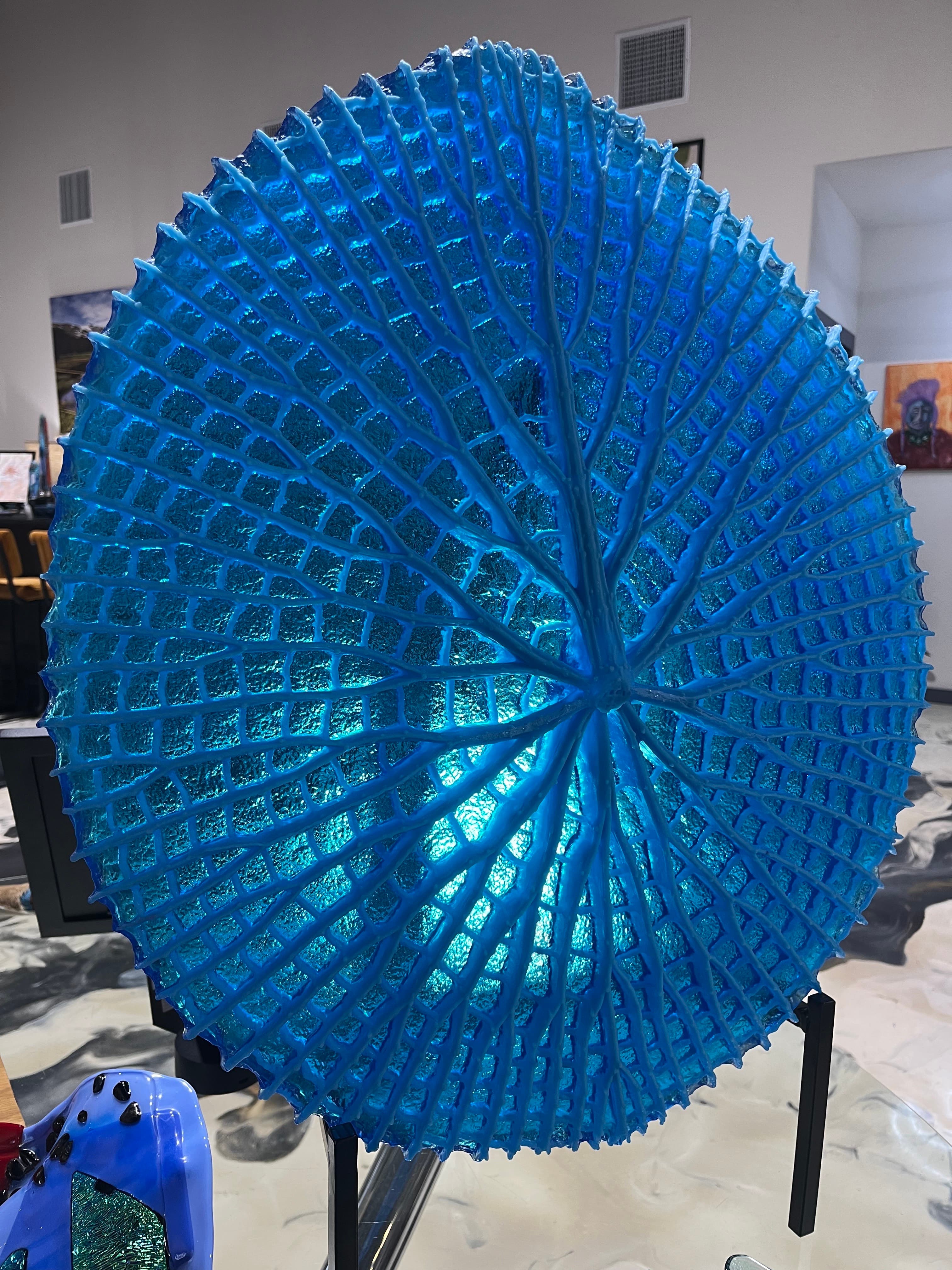 A luminescent blue glass sculpture resembling a sea urchin, displayed on a stand.