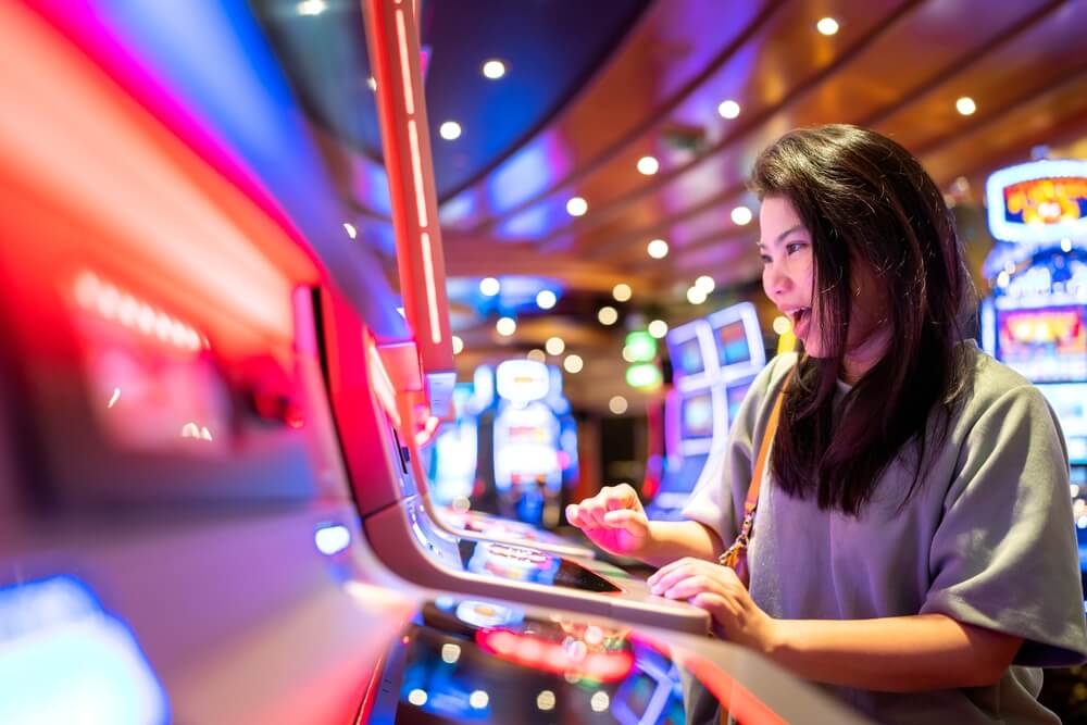 A woman smiles while playing a slot machine in a brightly lit casino. A woman smiles while playing a slot machine in a brightly lit casino.
