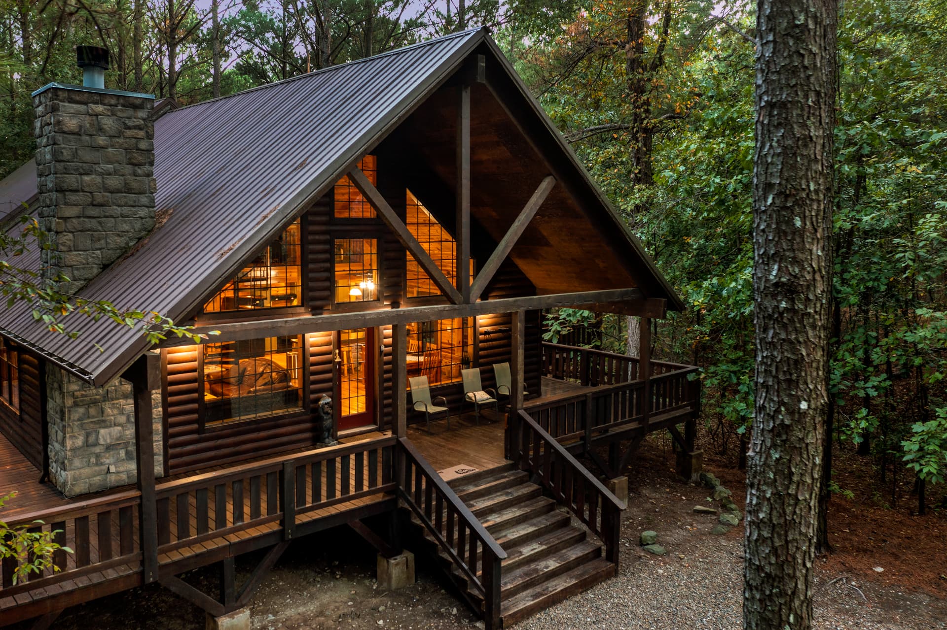 A cozy wooden cabin with a steep roof and large windows, surrounded by trees.