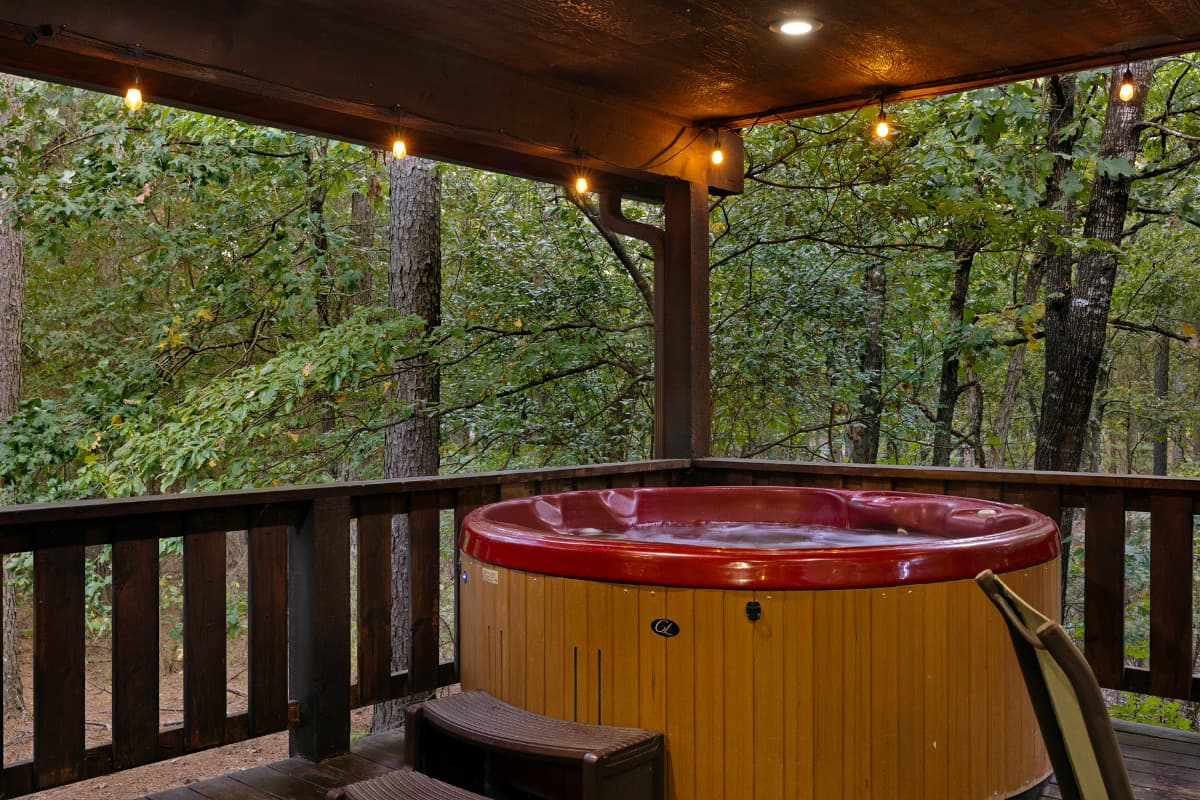 A wooden deck with a hot tub surrounded by lush greenery and string lights.