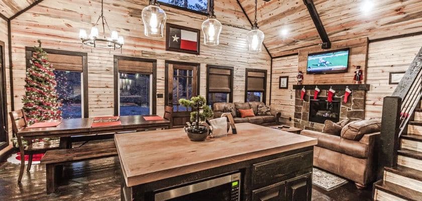 A cozy, rustic interior of a cabin featuring a dining area, a Christmas tree, and a fireplace.