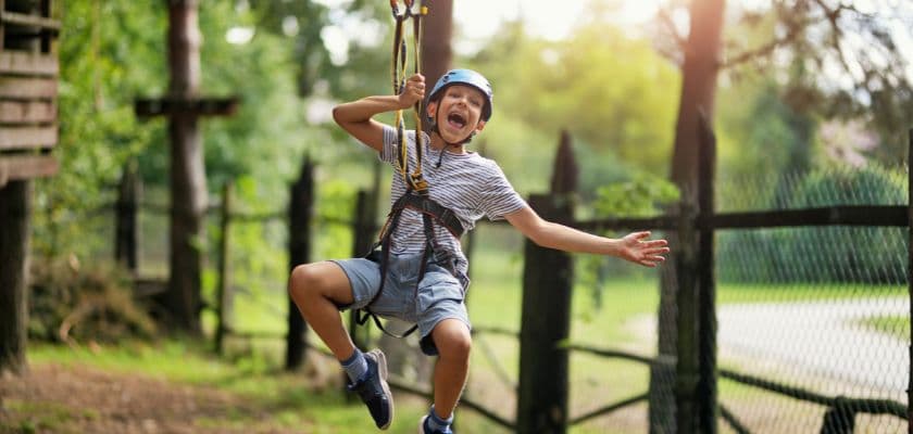 A joyful child in a helmet swings on a zip line.