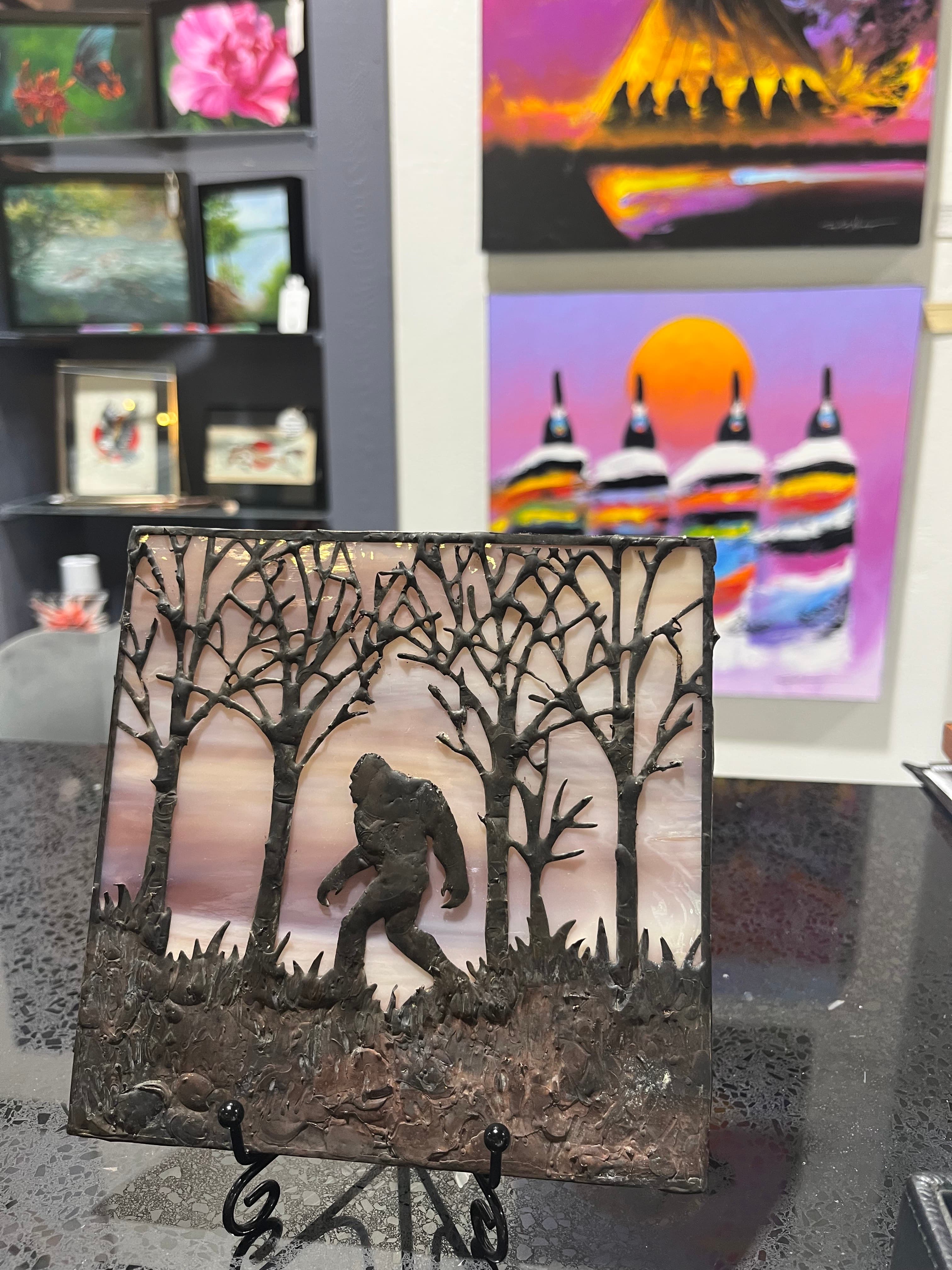A silhouette of a figure walking among trees, presented as a framed artwork, with colorful paintings in the background.