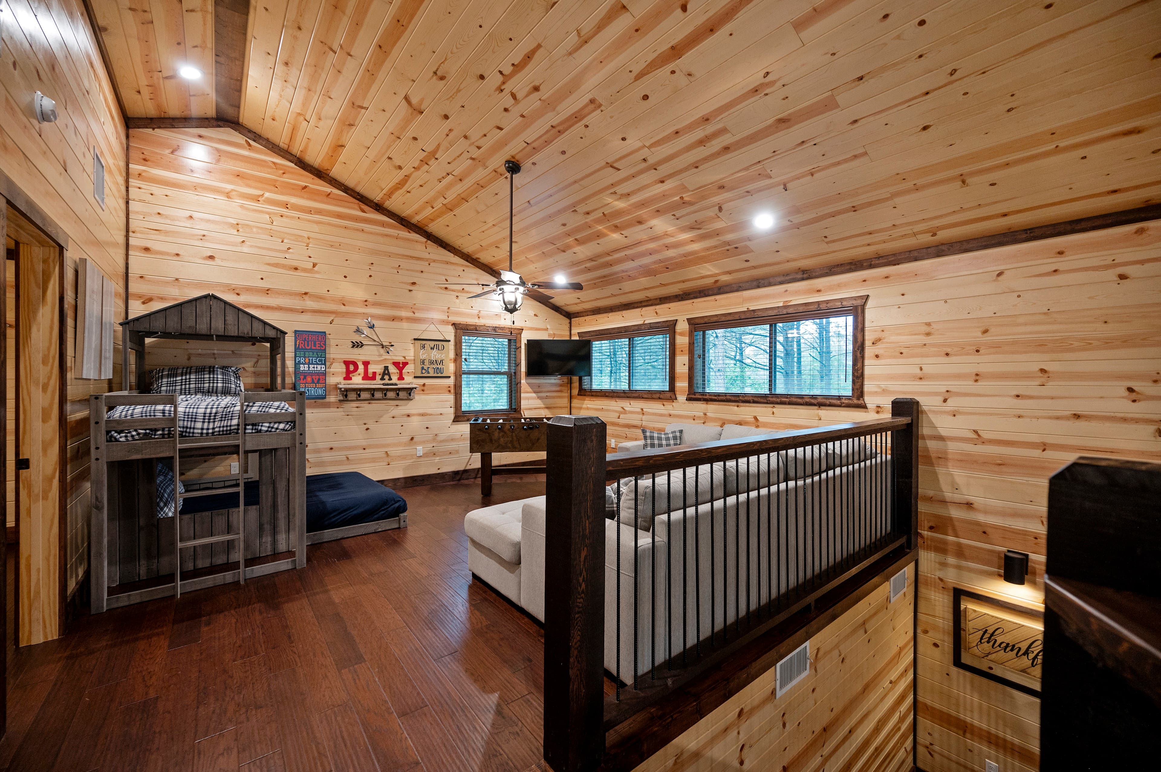 Lofted living space with wooden walls, plush seating, and large windows overlooking nature.
