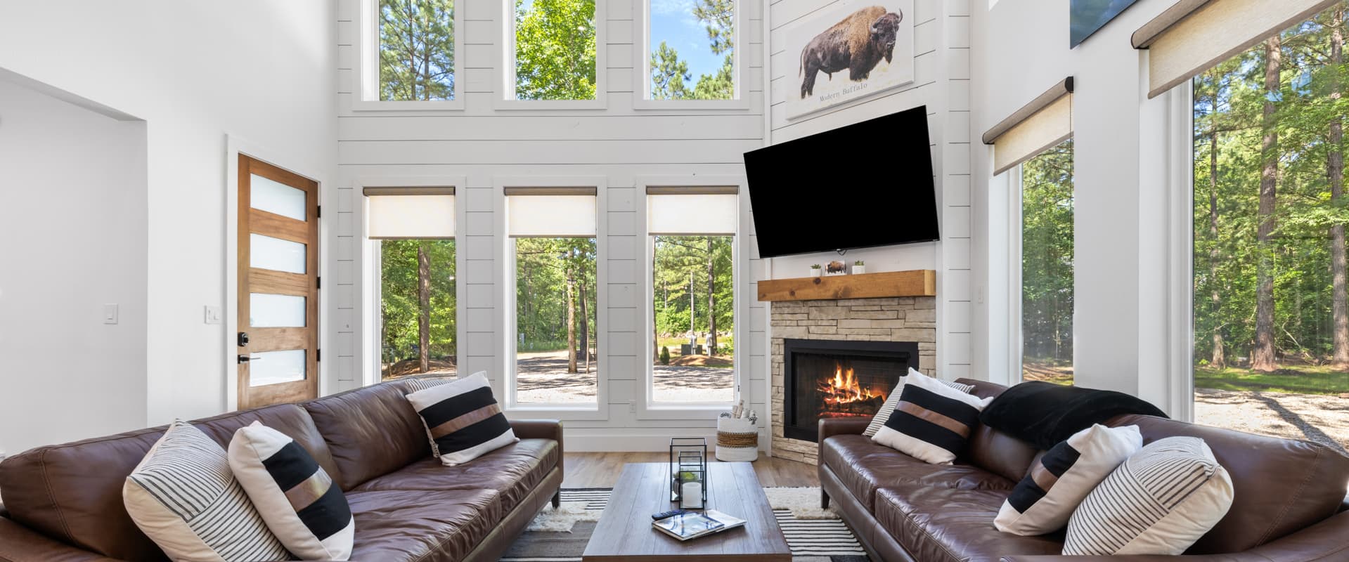 A modern living room featuring large windows, leather sofas, a fireplace, and a wooden door.