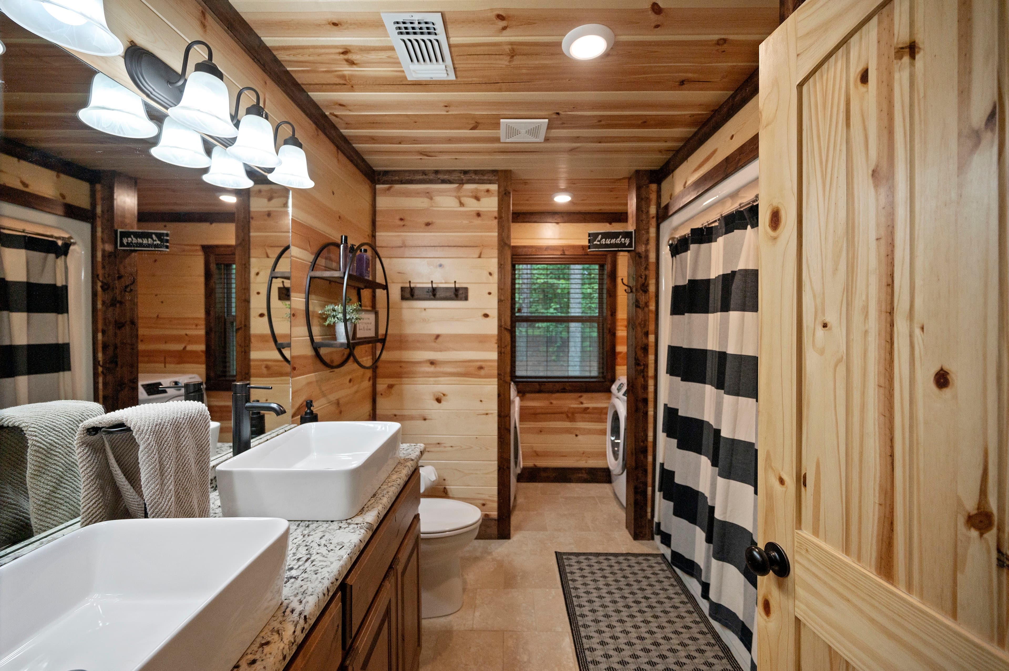 A rustic bathroom featuring wooden walls, dual sinks, and a black and white striped shower curtain.