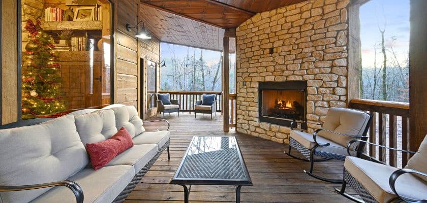 Cozy outdoor seating area with a stone fireplace and a Christmas tree in a rustic cabin setting.