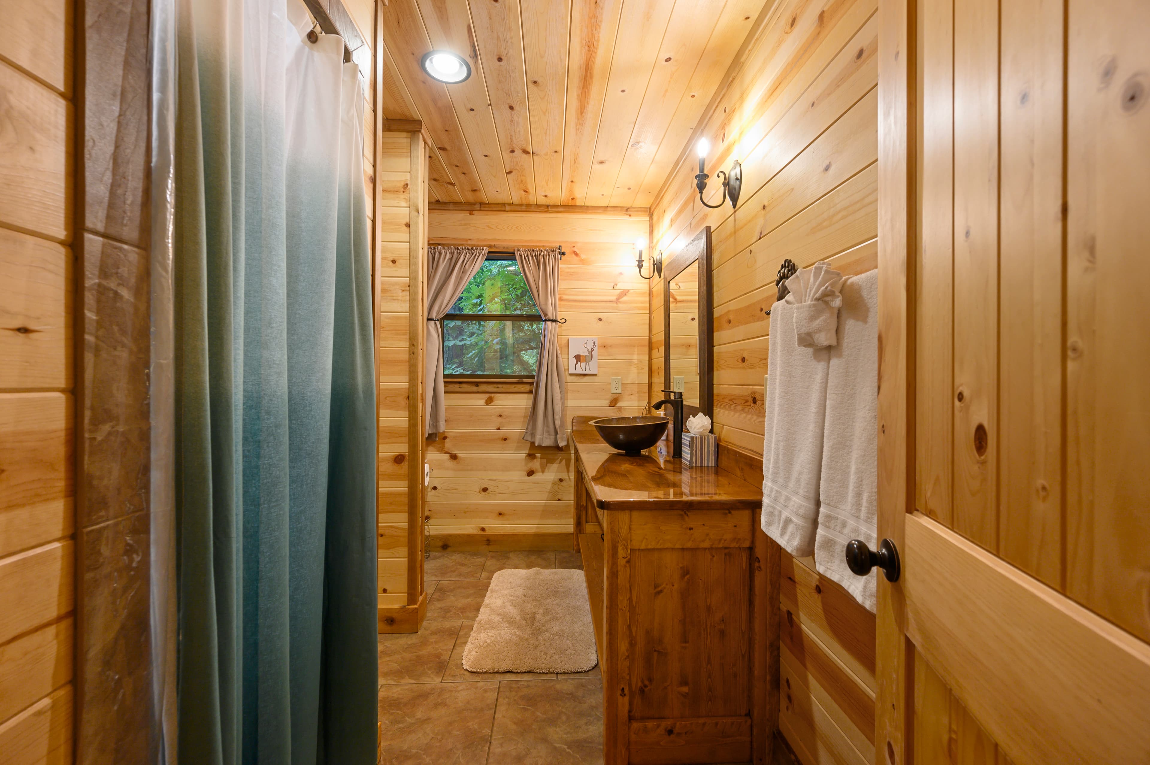 Cozy wooden bathroom featuring a sink, mirror, window, and shower curtain.