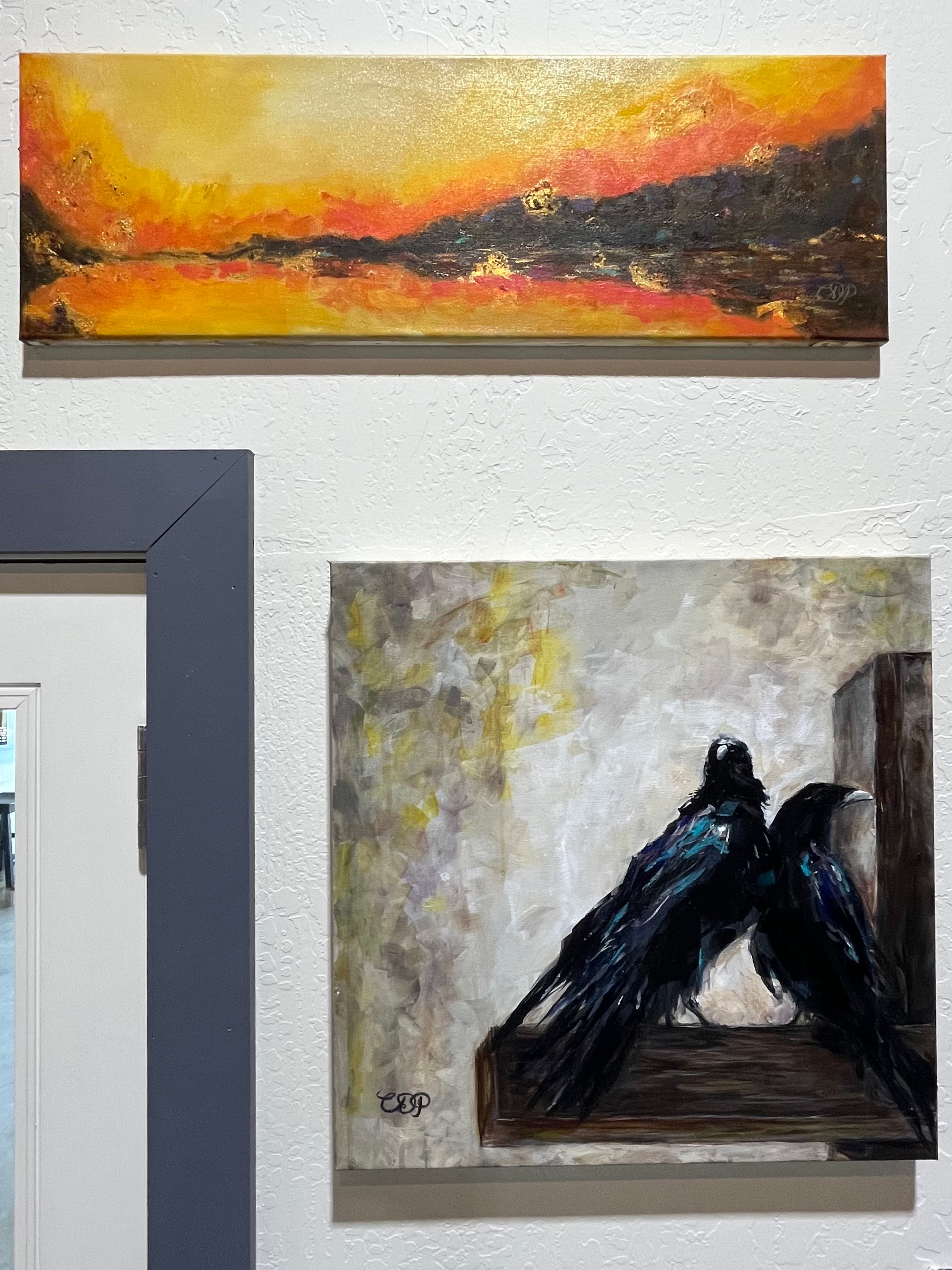 Two paintings are displayed on a wall: a horizontal abstract sunset above and a pair of black ravens below.