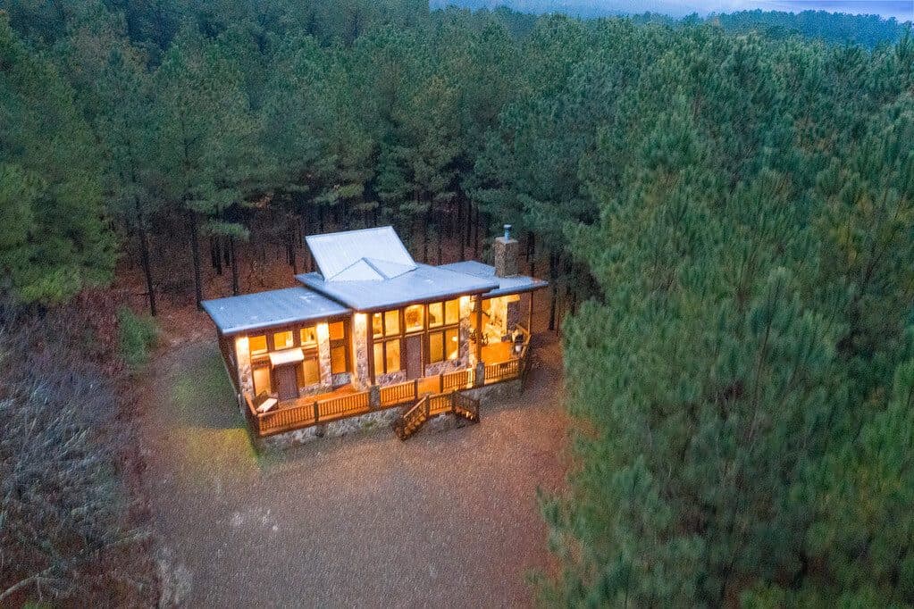 A modern cabin surrounded by tall trees at dusk.
