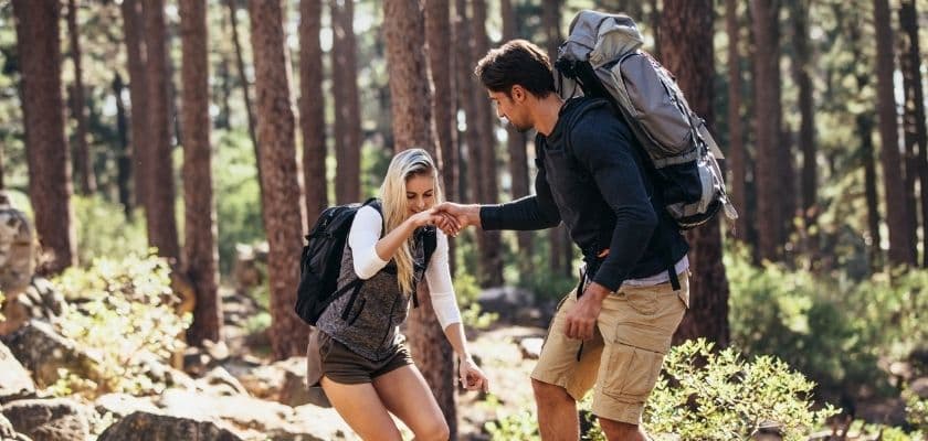 A couple holds hands while hiking a wooded trail.
