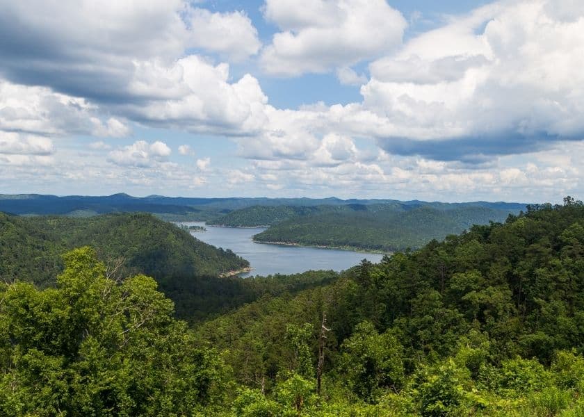 a scenic view of broken bow lake surrounded by lush green forested hills under a partly cloudy sky