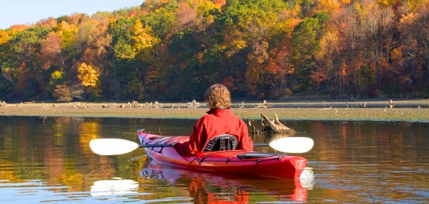 A person kayaking across Broken Bow Lake surrounded by colorful fall foliage.