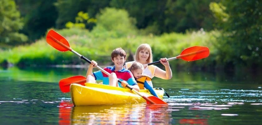 a family paddles a kayak on a calm lake surrounded by trees