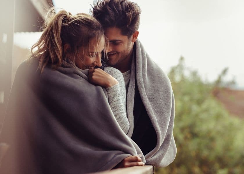 couple wrapped in a blanket outside cuddling and smiling at each other couple wrapped in a blanket outside cuddling and smiling at each other