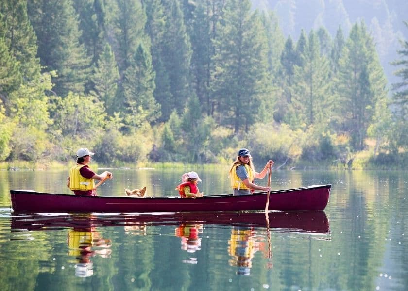 family canoeing on a calm lake surrounded by forest family canoeing on a calm lake surrounded by forest